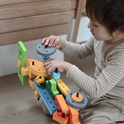 Criança a brincar com brinquedo de construção de madeira colorida no chão.