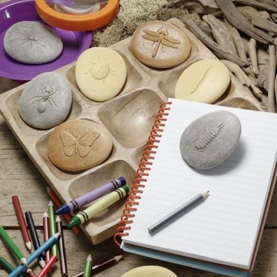 Pedras decorativas com relevo, lupa, lápis de cor e caderno numa mesa de madeira