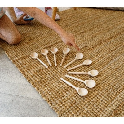 Dez colheres de madeira dispostas em leque num tapete castanho com criança a apontar