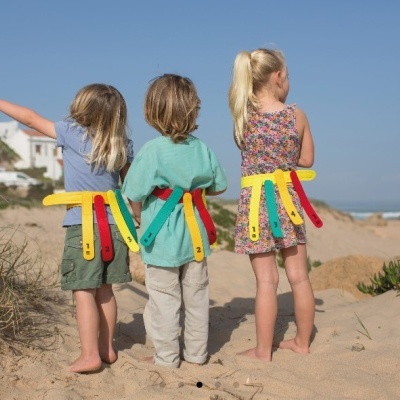 Três crianças de costas na praia com faixas coloridas e fitas coloridas nas cinturas
