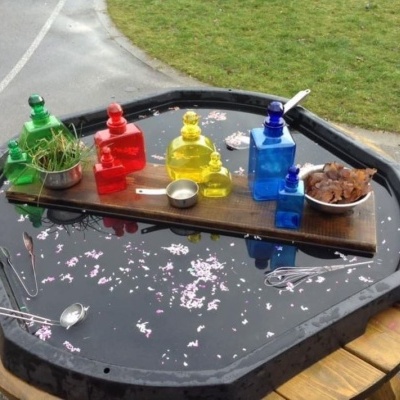 Mesa redonda preta com garrafas coloridas e objetos sobre tábua de madeira