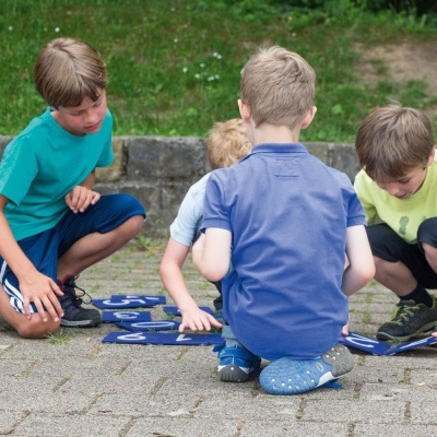 Quatro crianças sentadas no chão de pavimento a jogar com peças azuis