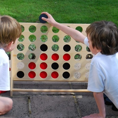 Duas crianças jogam jogo de tabuleiro de madeira com círculos vermelhos e pretos num jardim