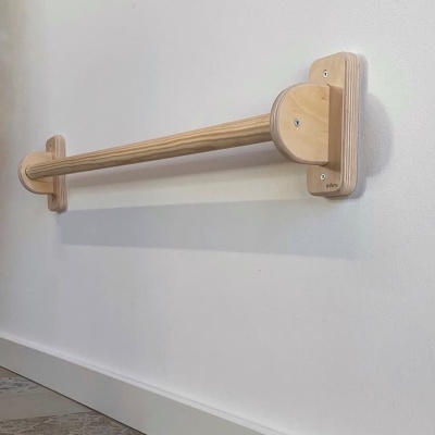 Barra de apoio de madeira clara fixa numa parede branca