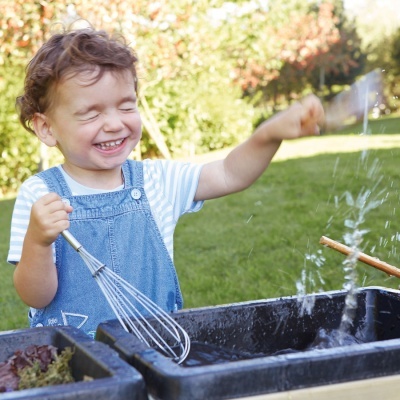 Criança com macacão azul a brincar com água fora de casa