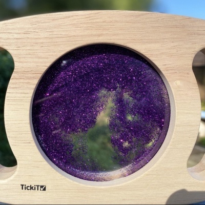 Objeto redondo com líquid roxo brilhante em moldura de madeira com logótipo TickiT