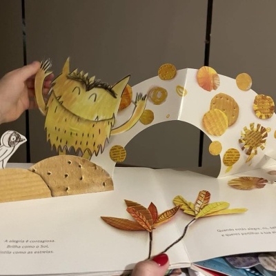 Livro pop-up infantil com monstro amarelo e folhas coloridas em relevo