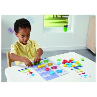 Menino a brincar com jogo educativo de tabuleiro com fichas coloridas numa mesa branca