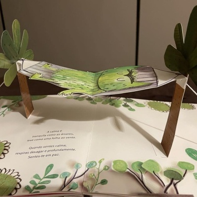 Livro infantil pop-up com ilustrações e recortes em papel de plantas e tronco verde