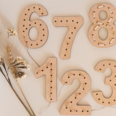 Números de madeira com buracos para fio e flores secas num fundo neutro