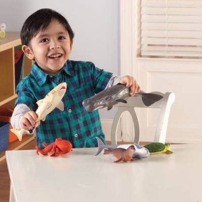 Menino a brincar com brinquedos de animais marinhos coloridos numa mesa branca