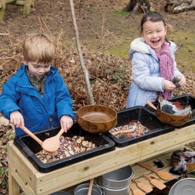 Crianças brincando com utensílios de madeira em mesa ao ar livre