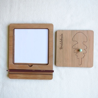 Quadro de madeira com suporte para papel e lápis, ao lado de placa com desenho de folha
