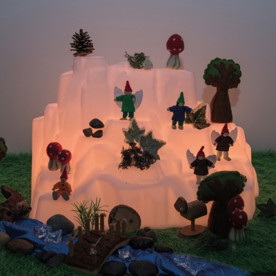 Miniatura decorativa com gnomos, cogumelos, árvores de feltro e musgo sobre montanha iluminada.