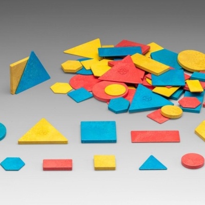 Peças geométricas de madeira coloridas em azul, amarelo e vermelho sobre superfície cinzenta