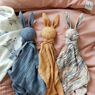 Três paninhos de bebé com cabeça de coelho azul, mostarda e marmoreado sobre tecido rosa