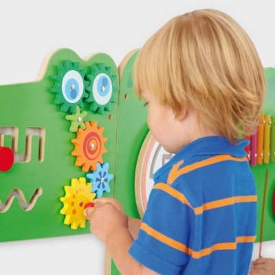 Criança a brincar com brinquedo educativo de parede em madeira colorida com engrenagens.