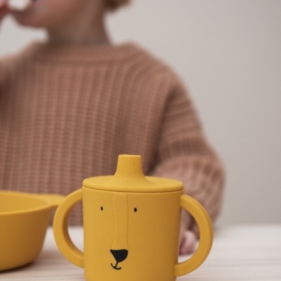 Copo infantil amarelo com tampa e dois pegas, com rosto de urso e tigela amarela ao lado