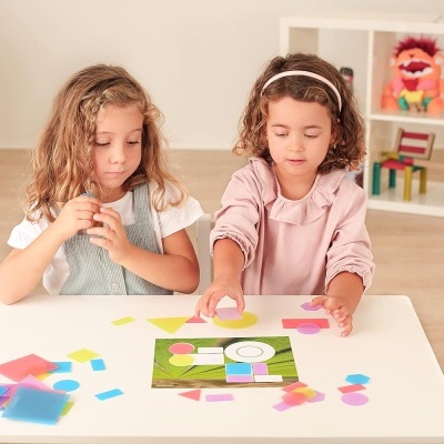 Duas meninas a brincar com peças de papel coloridas em formas geométricas numa mesa branca