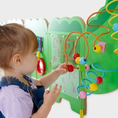 Painel educativo de parede em madeira verde com fios e contas coloridas, criança a brincar