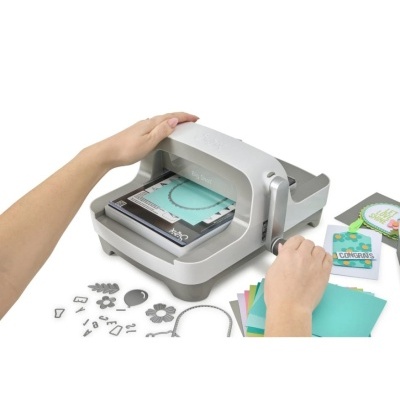 Máquina de corte manual Sizzix Big Shot com moldes metálicos e cartas coloridas.