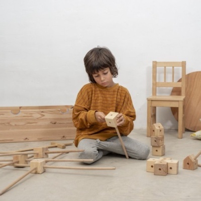 Criança a brincar com blocos de madeira clara no chão junto a cadeira de madeira
