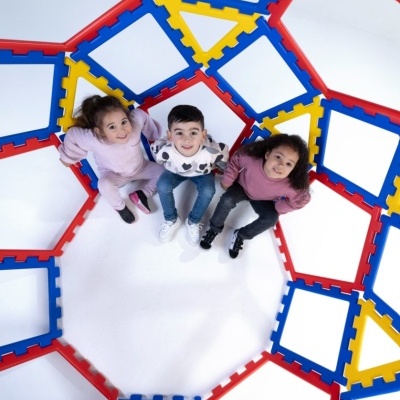 Três crianças sentadas rodeadas por molduras coloridas de plástico interligadas