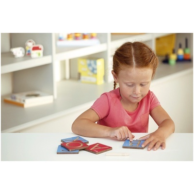 Criança a brincar com peças de madeira coloridas numa mesa branca em ambiente interior