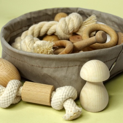 Brinquedos de madeira e corda numa cesta cinzenta sobre fundo verde claro