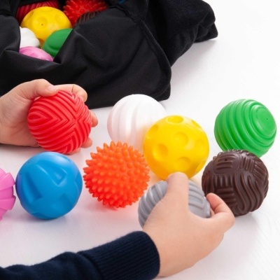 Bolas coloridas e texturizadas seguradas por mãos com saco preto ao fundo