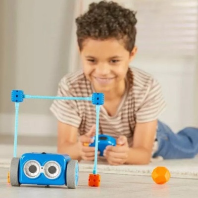 Criança a brincar com carro de brinquedo azul e cubos azuis com cordas, bola laranja na sala