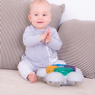 Bebé com roupa cinzenta e branca a brincar com brinquedo colorido sentado no chão