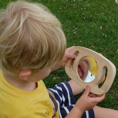 Criança segurando espelho com moldura de madeira na relva