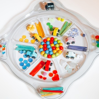 Organizador plástico transparente com divisórias contendo bolas, botões, palitos coloridos e mini carrinhos