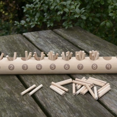 Jogo educativo de madeira com base numerada de 1 a 10 e pinos para encaixar, sobre mesa de madeira, ao ar livre