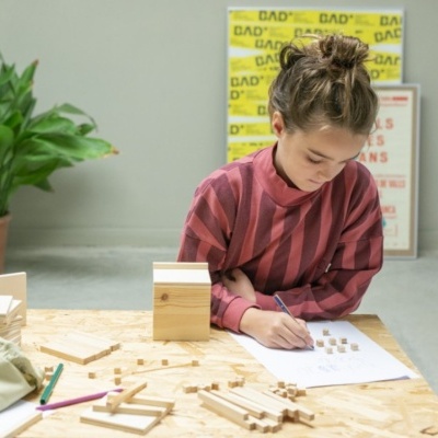 Criança sentada numa mesa com peças de madeira e uma planta no fundo