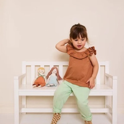 Menina sentada num banco branco de madeira com duas bonecas de tecido