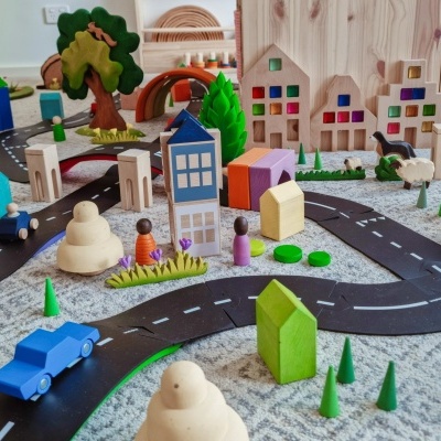 Brinquedos de madeira coloridos formando uma mini cidade com estrada num tapete cinzento