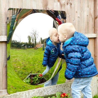 Menino de casaco azul a olhar para espelho convexo num jardim