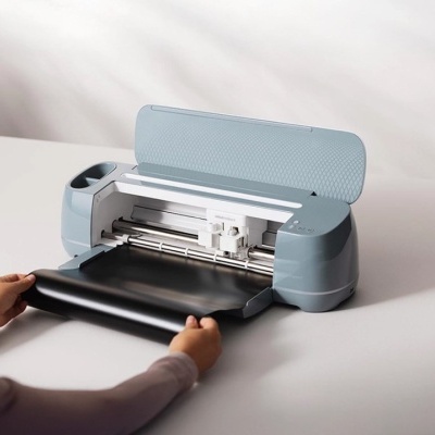 Máquina de corte eletrónica cinzenta a cortar vinil preto numa mesa branca