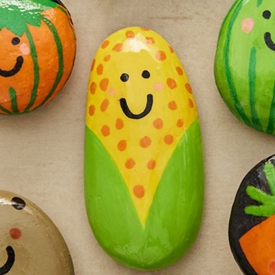 Pedras pintadas coloridas com rostos sorridentes e desenhos de frutas e legumes
