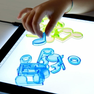 Peças de montagem plásticas azuis e amarelas transparentes sobre superfície iluminada com mão infantil