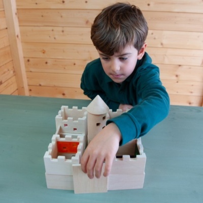 Menino a brincar com um castelo de madeira clara numa mesa azul