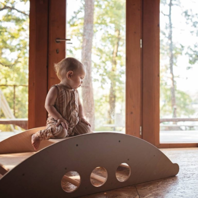 Bebé sentado em brinquedo de madeira cinzenta claro junto a janela grande de madeira