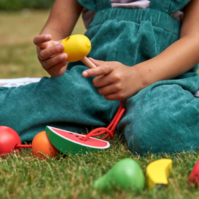 Criança a brincar com brinquedos de madeira coloridos em formas de frutas na relva