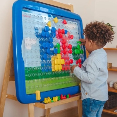 Quadro de pins coloridos numa estrutura azul com criança a brincar em ambiente interior