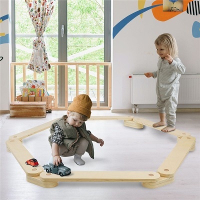 Dois bebés a brincar numa estrutura octogonal de madeira clara no chão de uma sala com janelas e decoração colorida