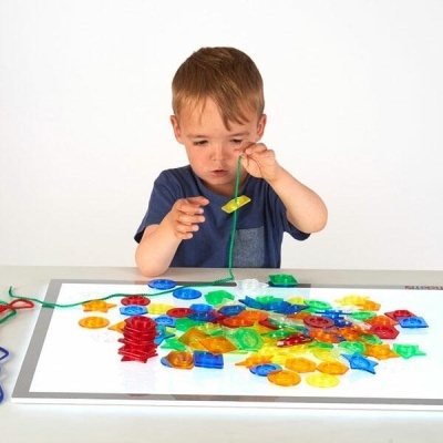 Criança a fazer colar com contas coloridas em mesa branca