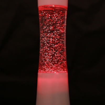 Lâmpada de lava com partículas vermelhas e base branca iluminada em fundo preto