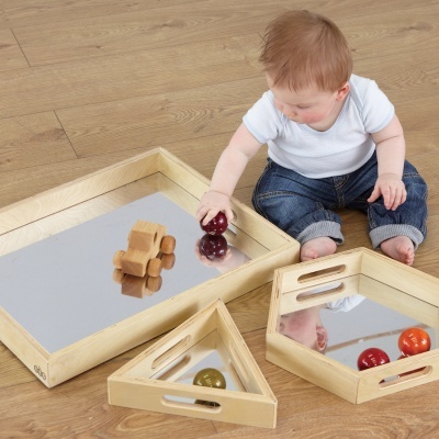 Tabuleiros de madeira com superfície espelhada e brinquedos, bebé sentado no chão de madeira